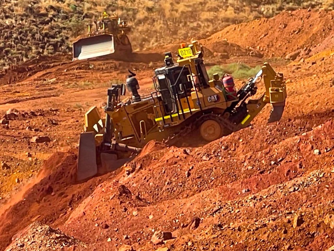 Two CAT dozers cutting a bench into red Pilbara dirt
