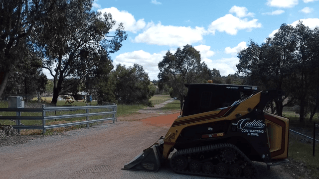 Signwritten Cadillac Contracting skid steer staged on a rural driveway under gum trees