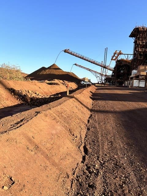 Drain reworked alongside an iron ore stockpile and conveyor at a port site