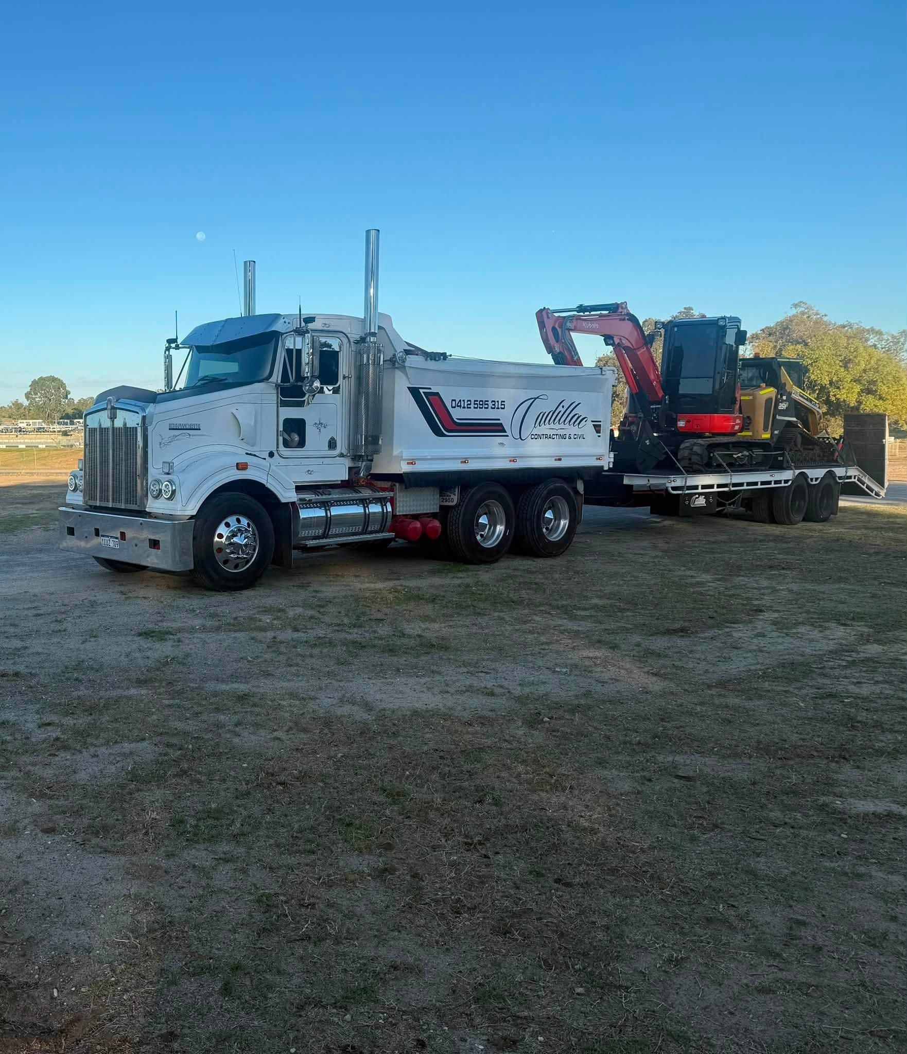 Tipper truck and low-loader float carrying an excavator and skid steer