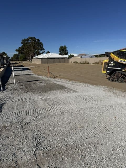 Skid steer spreading road base on a residential lot beside new houses